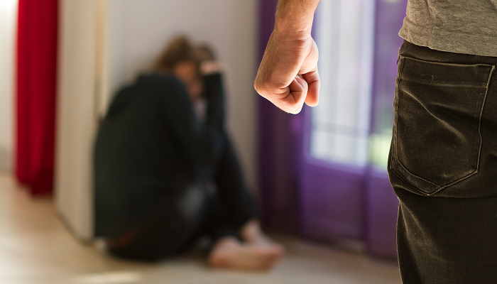 A person cowers in fear on the floor as another stands with a clenched fist, suggesting domestic violence
